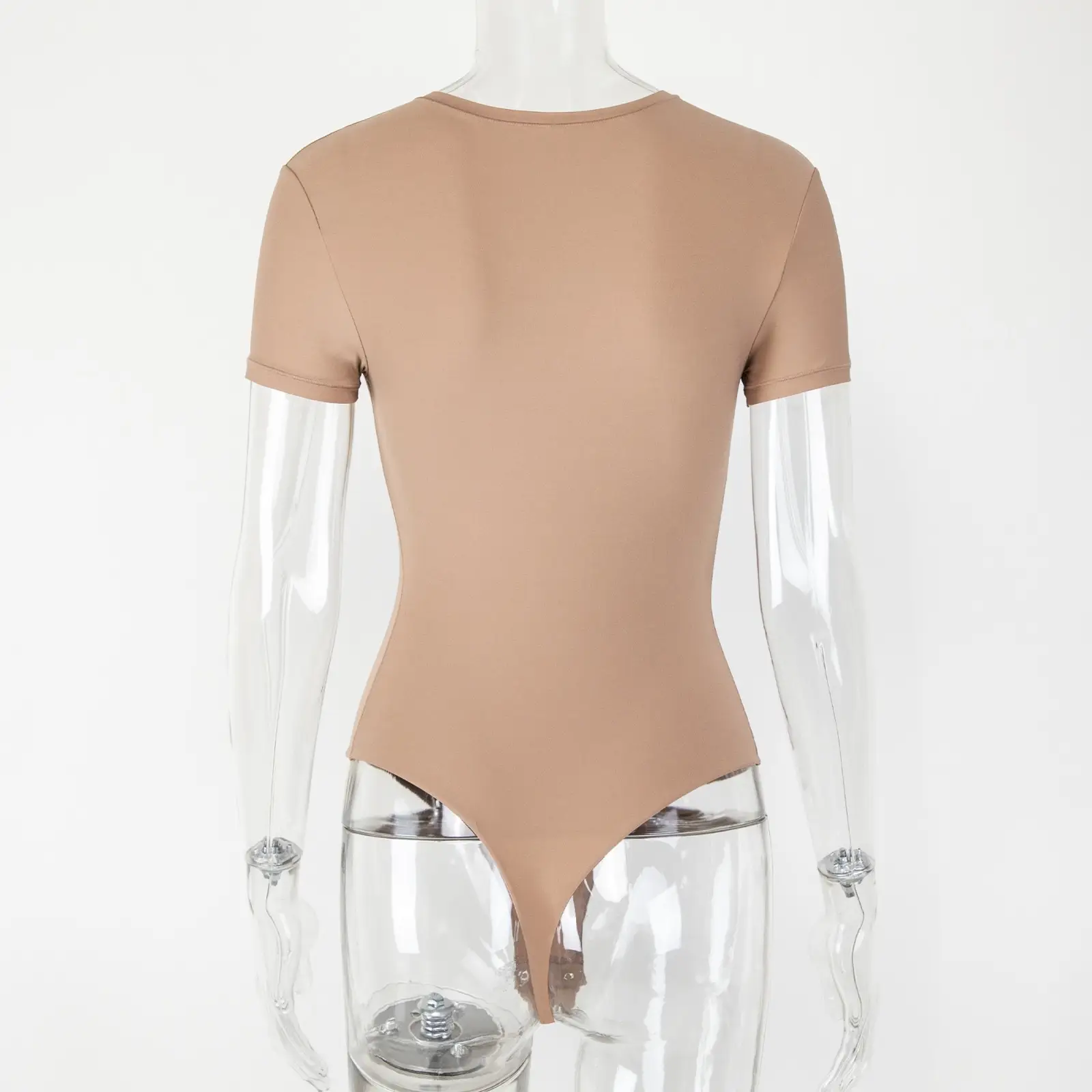 Transparent acrylic mannequin wearing a beige t-shirt bodysuit from the back over a white wall.