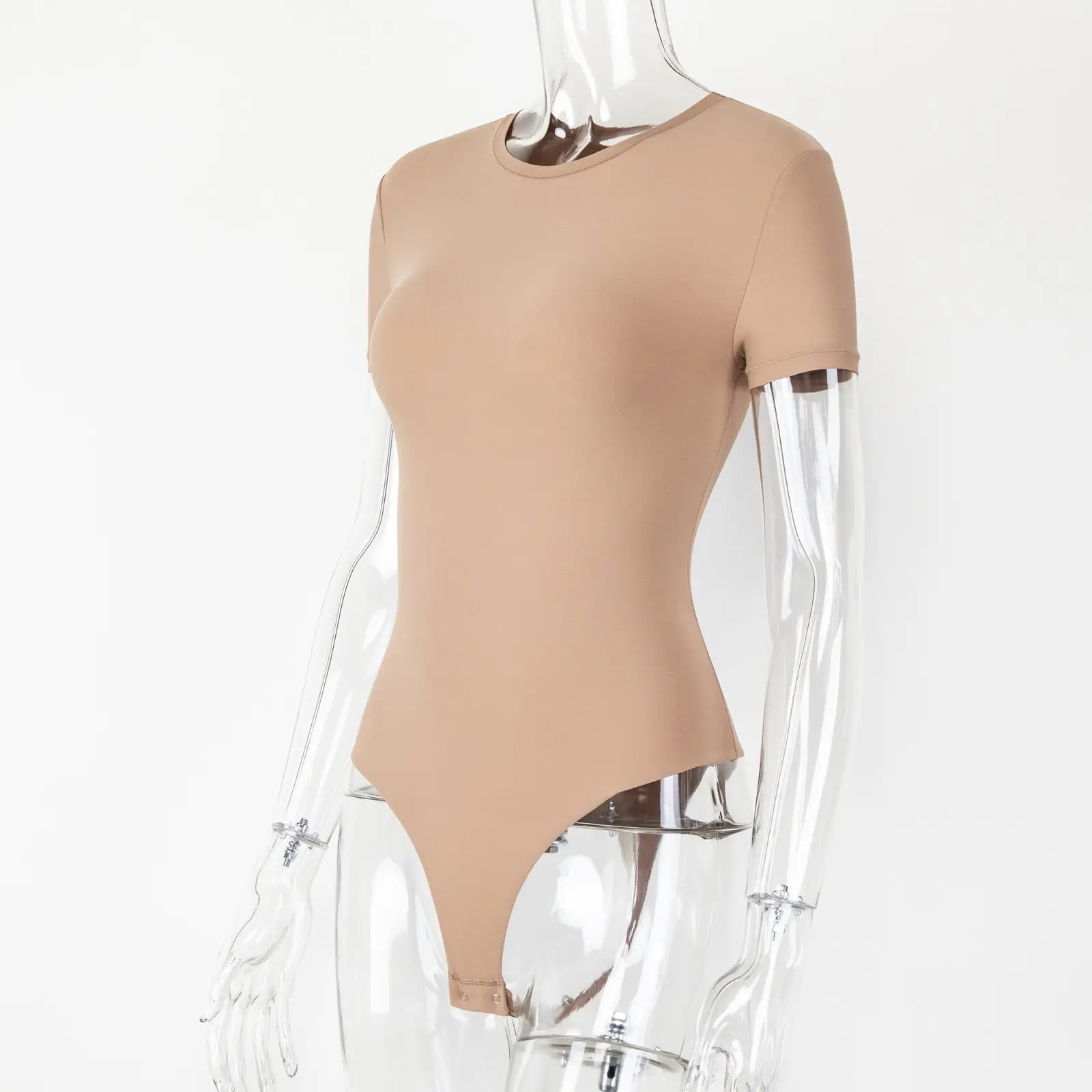 Transparent acrylic mannequin wearing a beige t-shirt bodysuit facing forwards with a white wall behind.