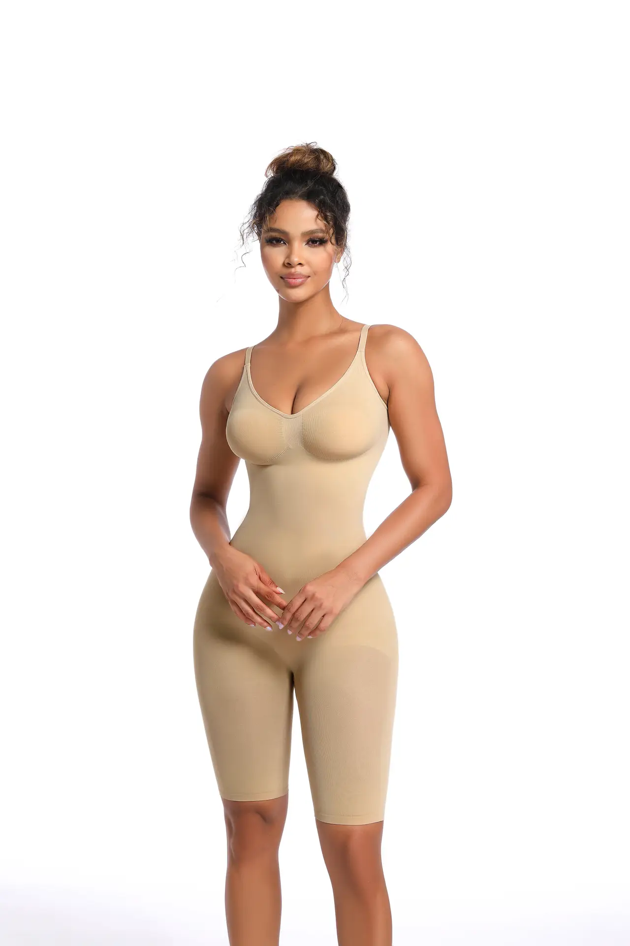 Mixed-race woman with her hair up, poses wearing a beige high-compression mid-thig bodysuit with a white background.