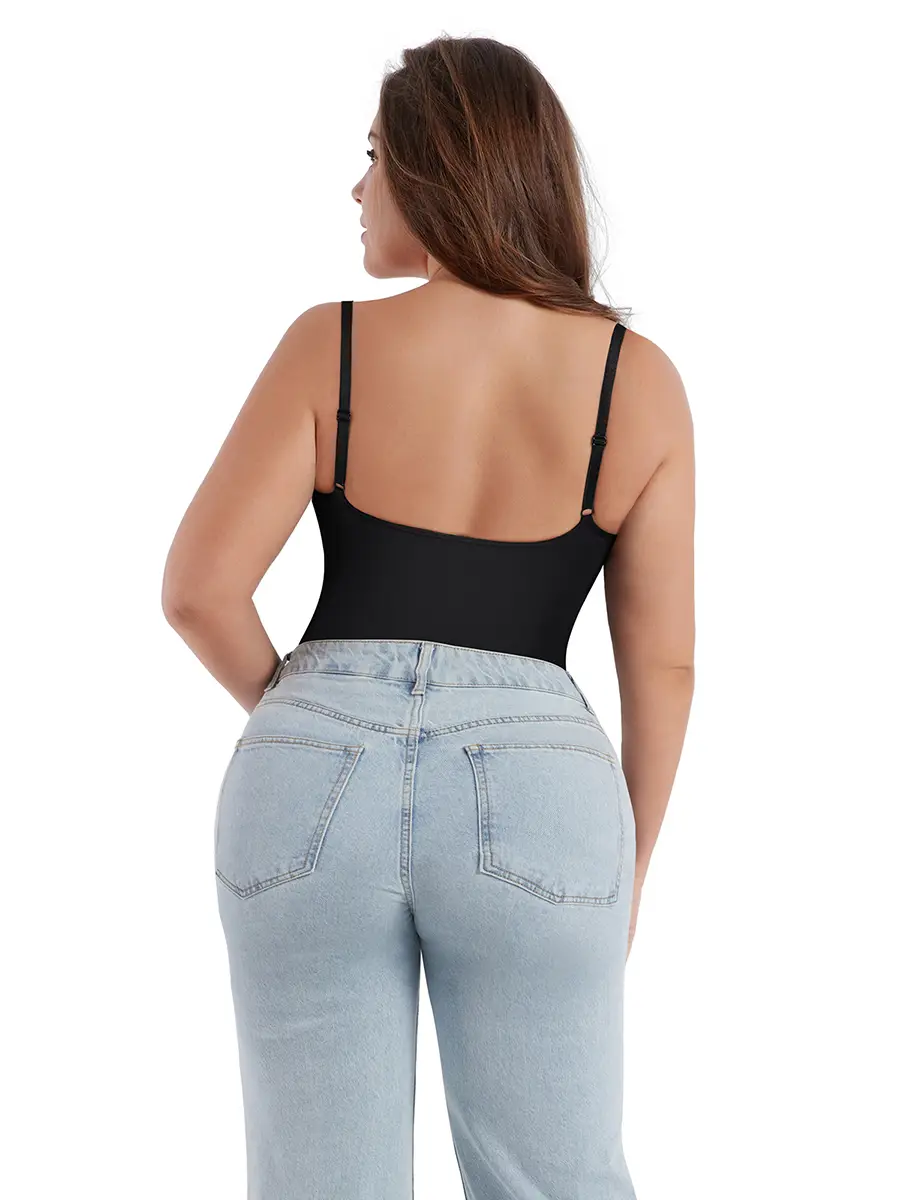 A woman with long brown hair, wearing a black spaghetti strap top and light blue jeans, stands with her back to the camera...